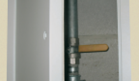White, fire rated access panel installed in wall, partly open hinged door revealing pipe work 