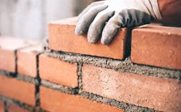 Man wearing safety gloves laying a course of brickwork